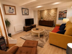 Ein Wohnzimmer mit einer Couch, einem Couchtisch, einem Fernseher, einer Steinwand und Kunstwerken an den Wänden.