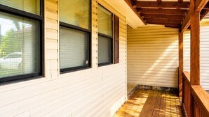 Eine überdachte Veranda mit Holzgeländern, einem Holzboden und einer weißen Außenwand mit Fenstern.