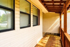 Eine überdachte Veranda mit Holzgeländern, einem Holzboden und einer weißen Außenwand mit Fenstern.