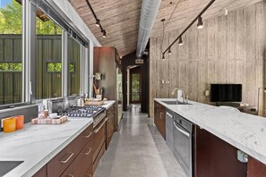 A modern kitchen with a long countertop, stainless steel appliances, and wooden cabinetry. - Midnight Hollow in Fennville (Fennville)