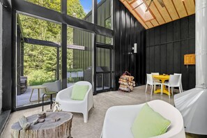 Ein modernes Interieur mit einer großen Schiebeglasdoor zum Außenbereich, einem Esstisch mit Stühlen und einer Sitzecke mit rundem Tisch und Stühlen.