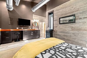 Ein modernes Schlafzimmer mit einem Bett, einem Schminktisch mit Spiegel, einem Fernseher und einem Stadtbild.