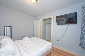 A bedroom with a bed, a television mounted on the wall, and a door leading to a bathroom. - Comfy & Convenient 2-Bed Fl 1 Apt @DowntownAlbany (Albany)