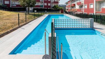 Una piscina rectangular amb terrassa enrajolada, envoltada per una tanca i edificis d'altes plantes a prop.
