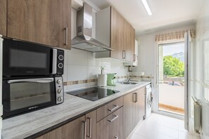 Una cocina moderna con microondas integrado, horno y lavaplatos. Se observa una ventana con vistas a zonas verdes y un coche fuera.