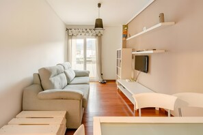 Un salón con sofá, televisión, escritorio blanco y ventana con cortinas.