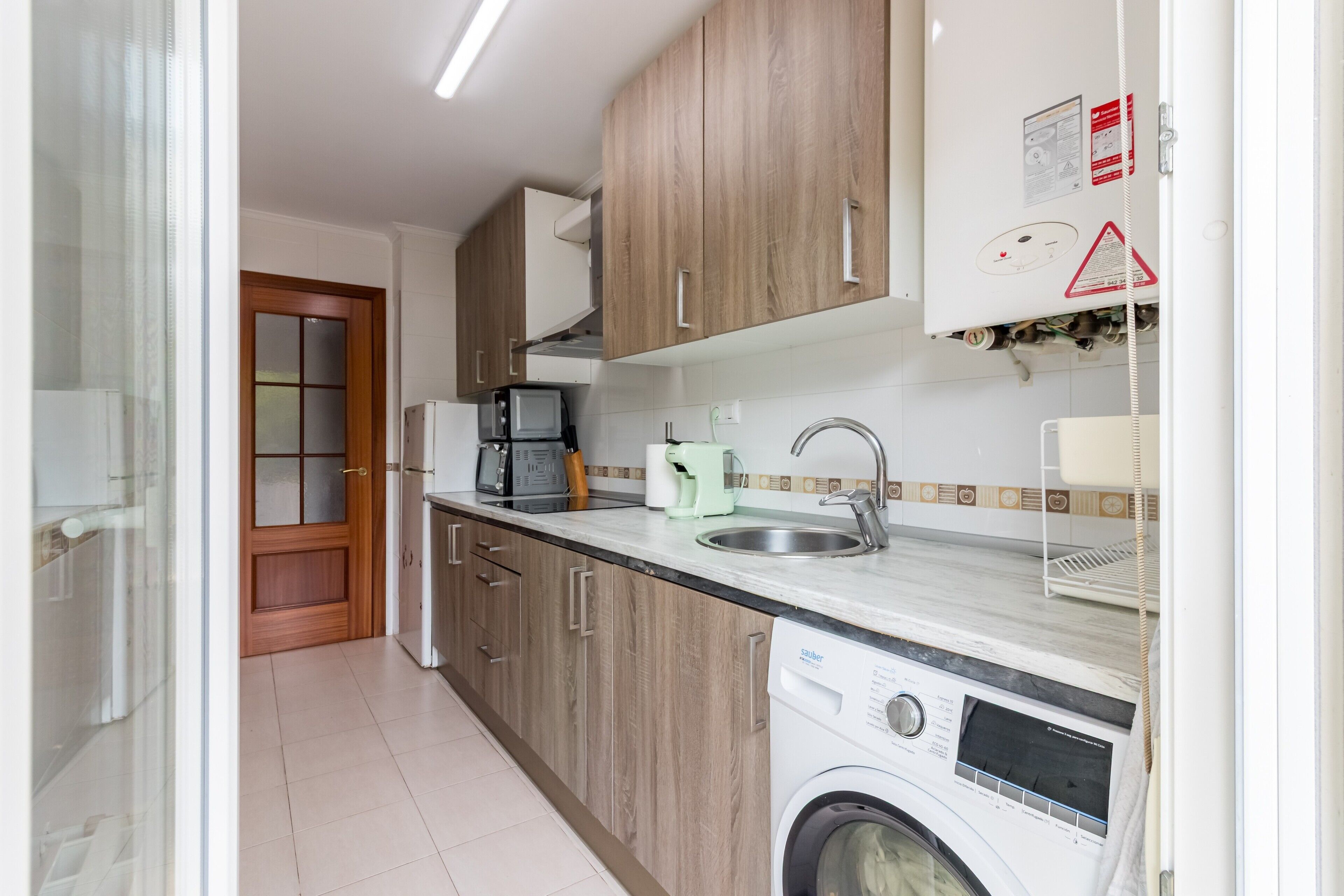 Una cocina con armarios de madera, lavadora, cafetera y microondas.