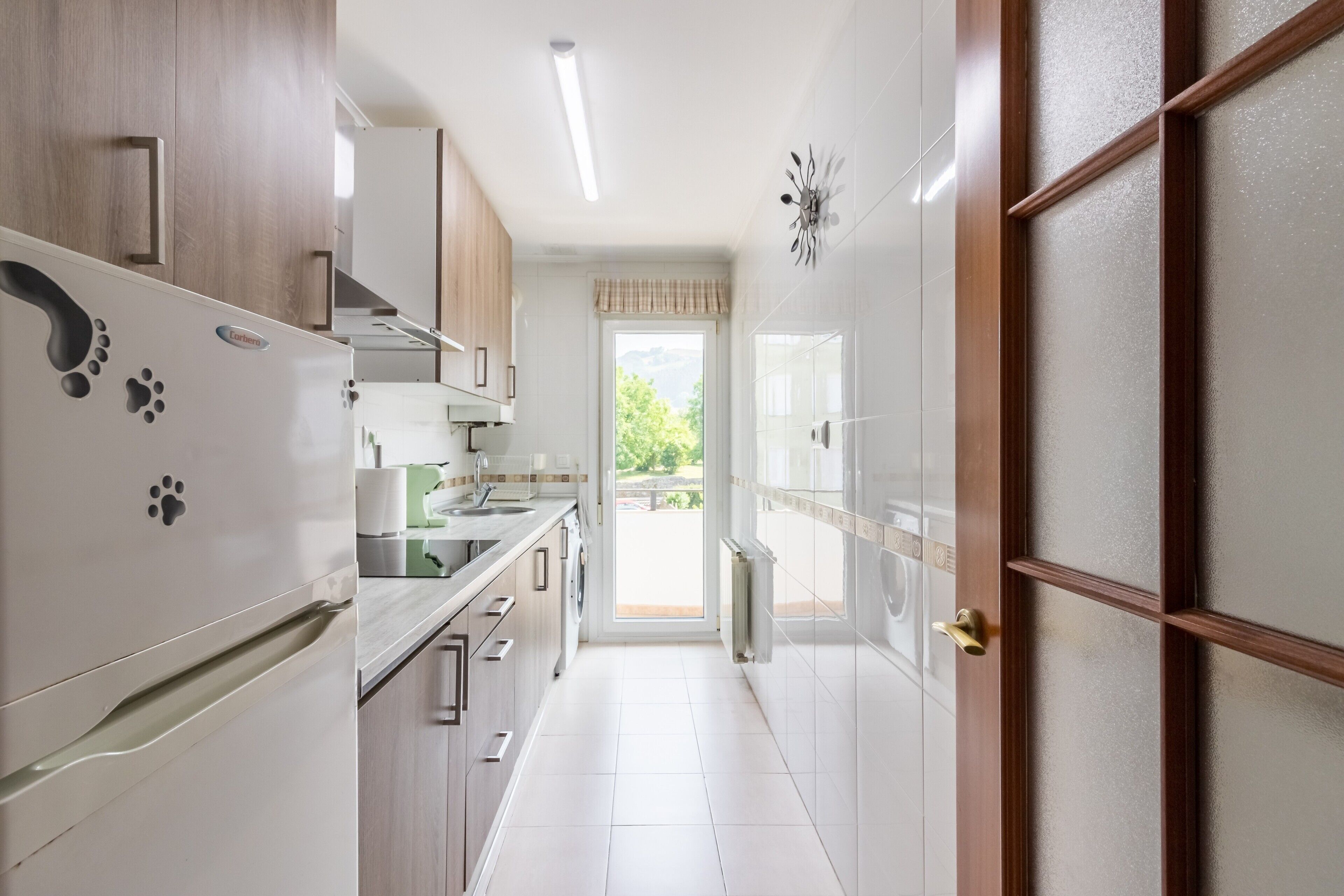 Una cocina con armarios blancos, un refrigerador y una ventana.