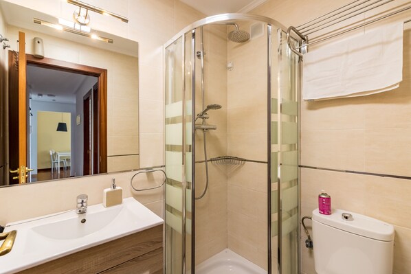 A modern bathroom with a glass-enclosed shower, a sink with a soap dispenser, and a toilet with a towel hanging on the wall.