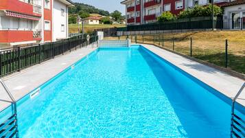 A rectangular swimming pool with clear blue water, surrounded by a black metal fence, and adjacent to a building with balconies.