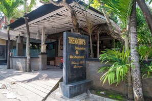 Une enseigne pour le restaurant « The Nicho's », avec un espace extérieur abrité et aménagé pour les clients, ainsi que des plantes tropicales.