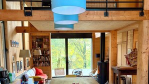 Una habitación amplia con una mesa de madera, una silla amarilla, una estantería y un ventanal con vistas a árboles.