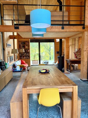 Ein geräumiges Zimmer mit einem Holztisch, einem gelben Stuhl, einem Bücherregal und einem großen Fenster mit Blick auf Bäume.