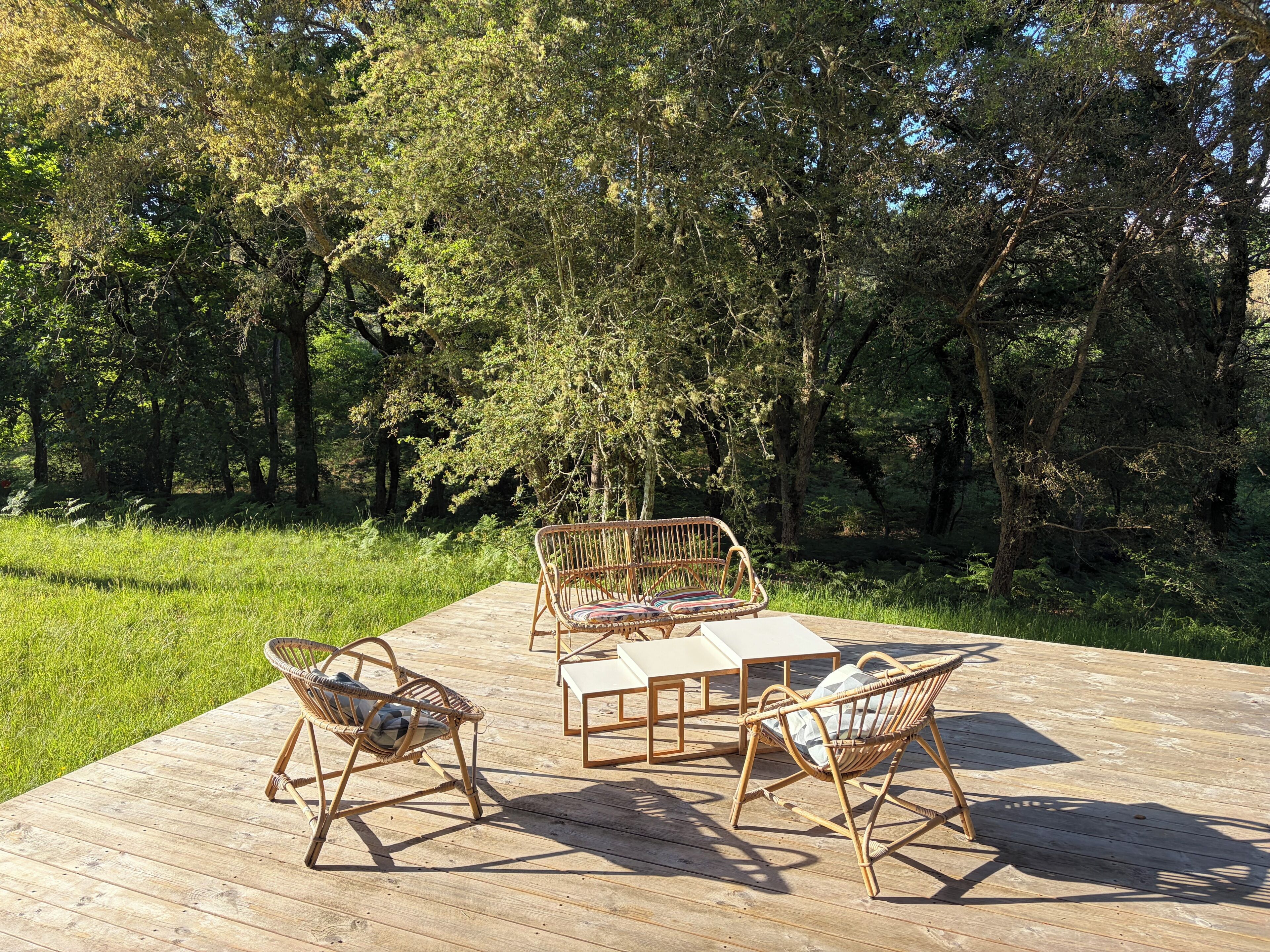 Een houten terras met rieten meubilair en een tafel, omgeven door een bos.