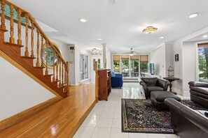 Un vaste espace de vie agrémenté d’un escalier en bois, d’un grand tapis, de canapés en cuir et offrant une vue à travers la porte vitrée.