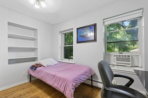 Une chambre à coucher avec un lit, une chaise, un radiateur et une fenêtre donnant sur des arbres.