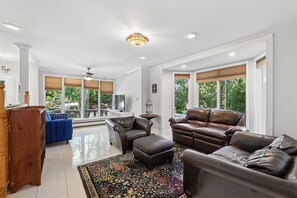 A spacious living room with a large window, a chandelier, and a blue sofa. - Beautiful 3 bedroom house minutes from NYC, Metlife, & American Dream Mall (Teaneck)