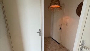 En hall med en vit dörr, en hängande lampa och ett klinkergolv.