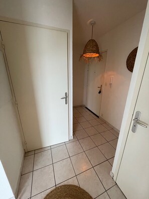 Ein Flur mit einer weißen Tür, einer Pendelleuchte und einem Fliesenboden.