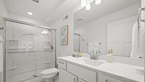 A modern bathroom with a glass-enclosed shower, a white sink with a large mirror, and a toilet.