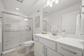 Et moderne badeværelse med en brusekabine i glas, en hvid vask med stort spejl og et toilet.
