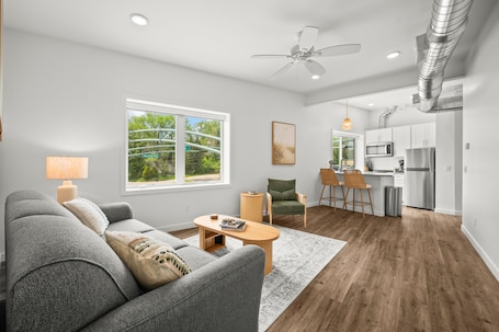 A modern living room with a sofa, coffee table, and chairs, a kitchen with white cabinets and appliances, and a large window with a view of trees.. 1 BR King Suite - Freshwater Inn - Bridgman, MI - Unit 1