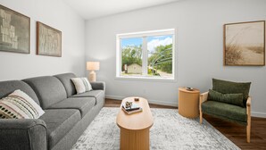 A modern living room with a grey sofa, a wooden coffee table, a green armchair, and a large window with a view of greenery.