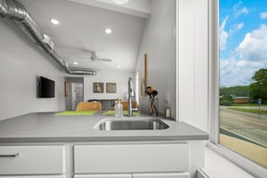 A modern kitchen with a large window, a built-in sink, and a ceiling fan.