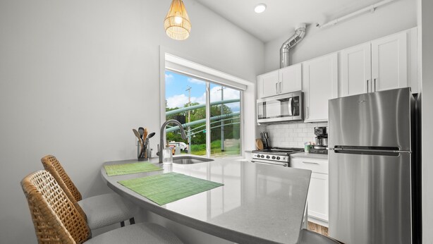 A modern kitchen with white cabinets, stainless steel appliances, a large island with seating, and a view of greenery outside.