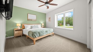A bedroom with a bed, nightstands, a ceiling fan, a window, and artwork on the walls.