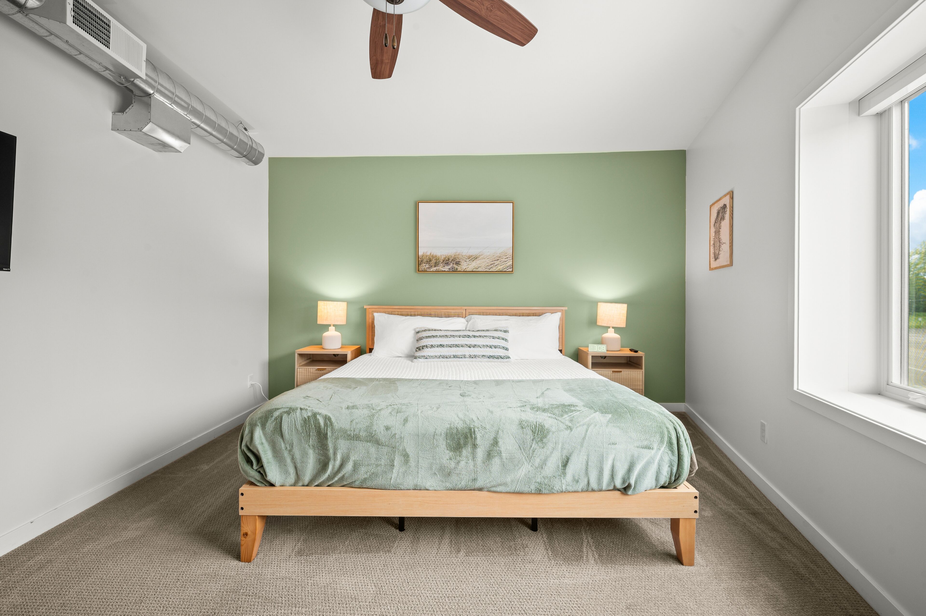 Een slaapkamer met een bed, twee bedlampen, een plafondventilator, een raam en een aan de muur bevestigd schilderij.