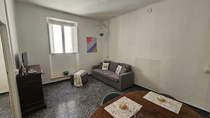 Ein Wohnzimmer mit einer Couch, einem Tisch mit Platzsets, einem Fenster und einer Wanddekoration.