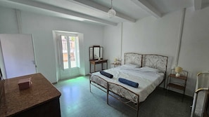 Une chambre à coucher comprenant un lit, des tables de chevet, un bureau et une porte donnant sur un espace extérieur.