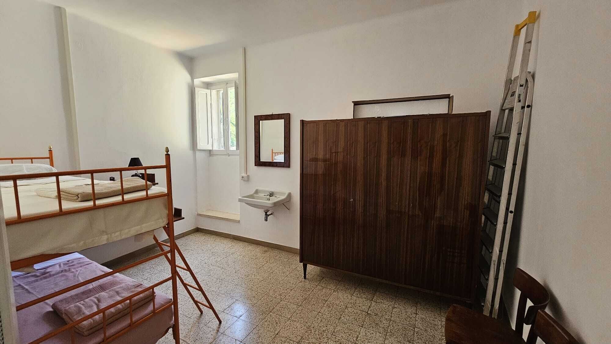 A room with bunk beds, a wooden wardrobe, a small sink, and a window with curtains.