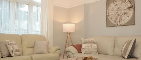 Un salón con un sofá color beige, una mesa de centro de madera y una lámpara de pie.