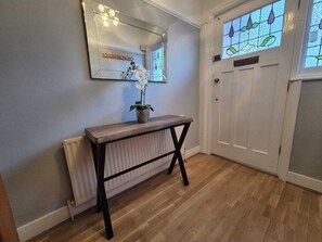 A hallway with a wooden console table, a mirror, a potted orchid, and a door with stained glass. - Palmers Green | 3BDR | Entire House | Relocation (London)