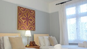 Ett hotellrum med två sängar, ett nattduksbord med en lampa, en dekorativ väggdekoration och ett fönster med gardiner.
