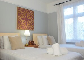 A hotel room with two beds, a nightstand with a lamp, a decorative wall piece, and a window with curtains. - Palmers Green | 3BDR | Entire House | Relocation (London)