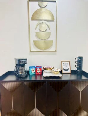 A coffee station with a coffee maker, cups, and a sign.