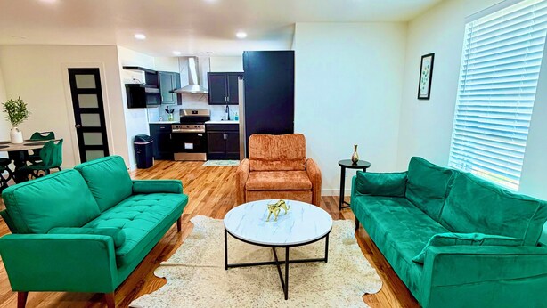 Una sala de estar con dos sofás verdes, una mesa de centro redonda y una cocina al fondo.