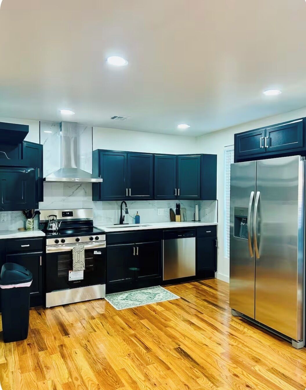 A modern kitchen with dark cabinets, stainless steel appliances, and a wooden floor.. Spacious Modern Glam House Minutes To Downtown