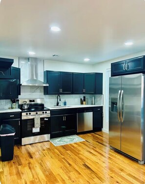 A modern kitchen with dark cabinets, stainless steel appliances, and a wooden floor. - Spacious Modern Glam House Minutes To Downtown (Oklahoma City)
