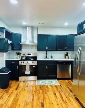 A modern kitchen with dark cabinets, stainless steel appliances, and a wooden floor.