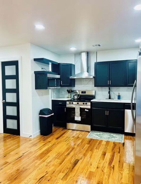 A modern kitchen with black cabinets, stainless steel appliances, and a wooden floor.