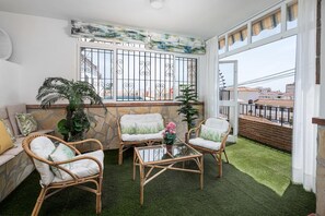 En balkon med fletningsmøbler, en stenvæg og udsigt til bygninger.