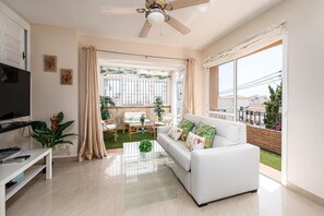 A modern living room with a white sofa, a glass coffee table, and a ceiling fan. - Casa Burriana – zonnig en gezellig verblijf op 5 min. lopen van het strand. (Nerja)