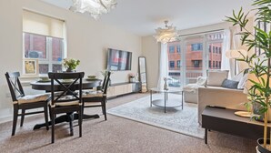 A modern living room with a dining area, large windows, and a view of a brick building. - Relocation | Coventry | Early Booking Discount (Coventry)