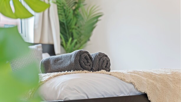 A neatly made bed with a rolled blanket, a beige throw blanket, and a white pillow. - Relocation | Coventry | Early Booking Discount (Coventry)
