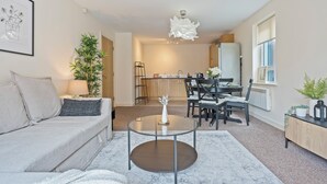 A modern living room with a sofa, coffee table, and a dining area with chairs and a table. - Relocation | Coventry | Early Booking Discount (Coventry)