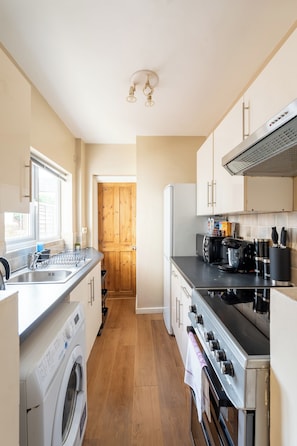 A compact kitchen with a washing machine, a stove, and a coffee maker. - Reading | 3 Bedrooms | Relocation | Long Stays (Reading)